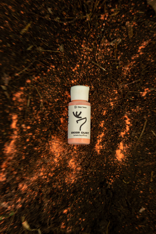 Deer Dust laying in a mock scrape with the powder in the scrape. The bottle has a white cap and a white label with black text and a deer logo. Synthetic mock scrape attractant.